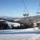 Widok na stok narciarski oraz wyciąg krzesełkowy na którym są 2 osoby z nartami.