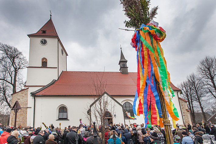 Duży kościół o białych ścianach z wieża. Procesja z wysokimi palmami.